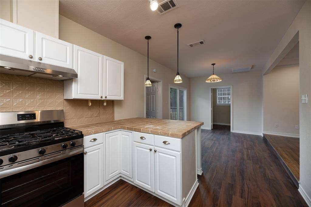 8823 San Benito Way, Dallas, TX 75218 Kitchen featuring white cabinetry, tile backsplash, built-in gas range, and a breakfast bar with tile countertop
