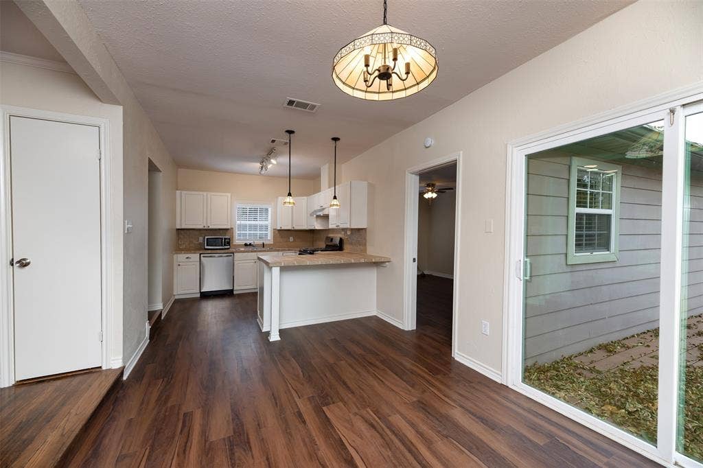 8823 San Benito Way, Dallas, TX 75218 Wood-finish flooring throughout, white cabinetry, integrated stainless steel appliances, breakfast bar, and sliding glass door
