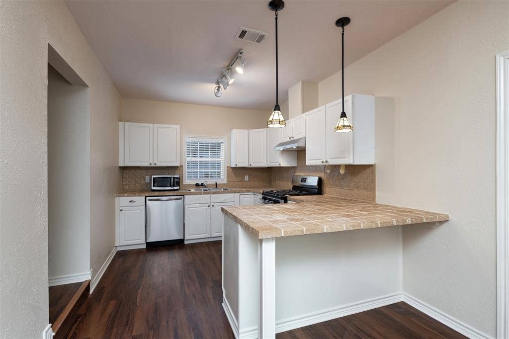 8823 San Benito Way, Dallas, TX 75218 Kitchen featuring white cabinetry, wood-finish flooring, stainless steel dishwasher, a gas range, and a tile backsplash