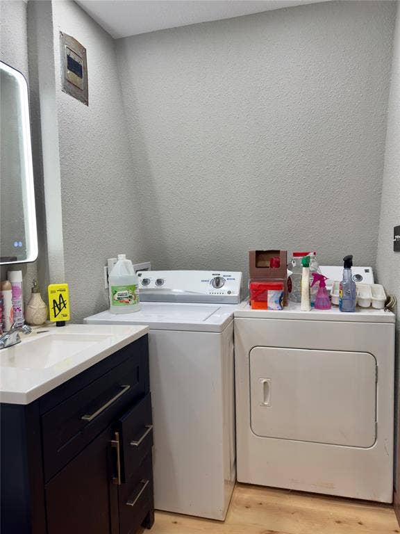 157 Business Boulevard, Granbury, TX 76049 Laundry area featuring separate washer and dryer, a textured wall, a sink, and light wood-type flooring