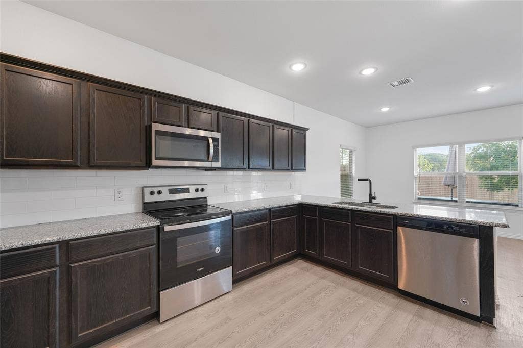 4651 Raleigh Dalton Road, Dallas, TX 75227 Modern kitchen featuring dark cabinetry with raised-panel doors, stainless steel appliances including a slide-in range and over-the-range microwave, quartz countertops, subway tile backsplash, and light wood-finish flooring