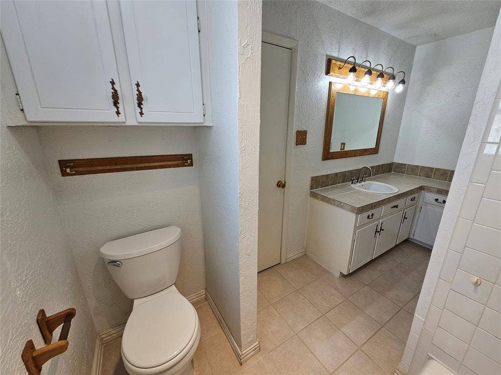 1109 W Redbud Drive, Hurst, TX 76053 Built-in vanity with integrated sink, tile countertop, and mounted mirror with overhead lighting