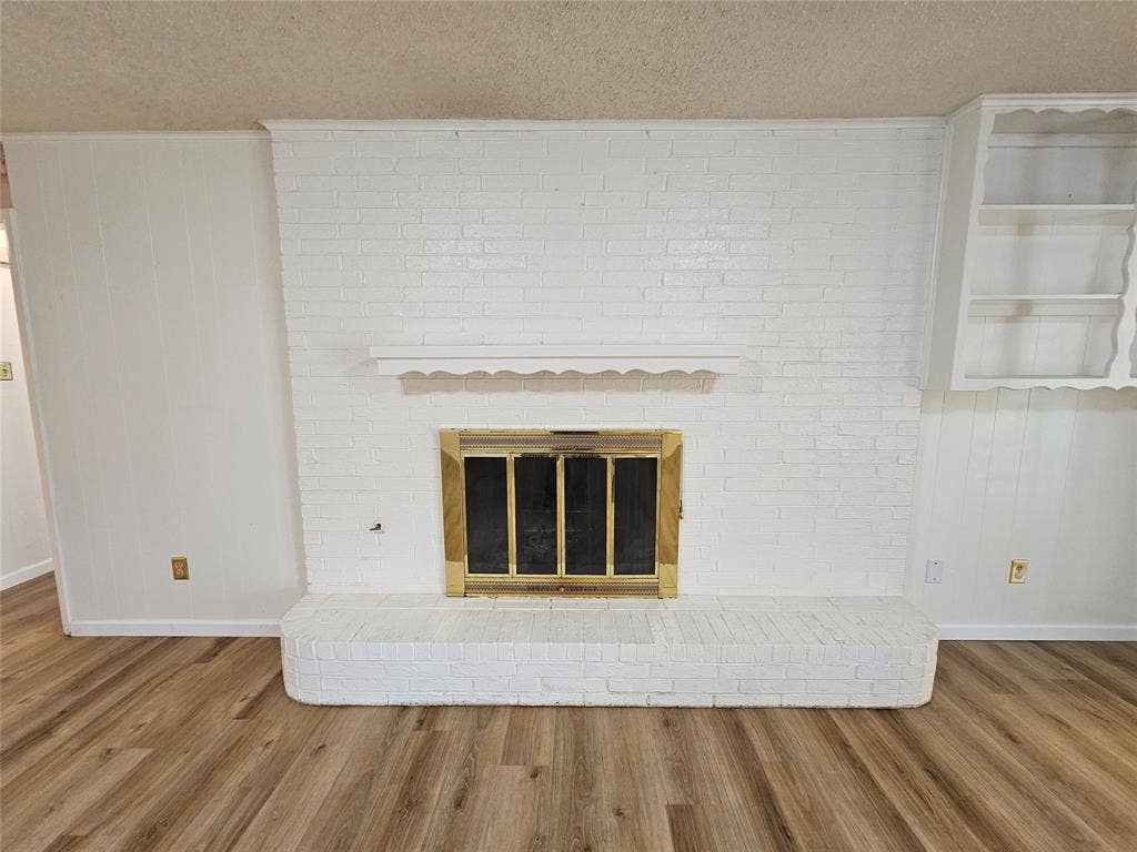 1109 W Redbud Drive, Hurst, TX 76053 Brick fireplace with brass firebox, built-in shelving, wood-finish flooring, and painted paneling