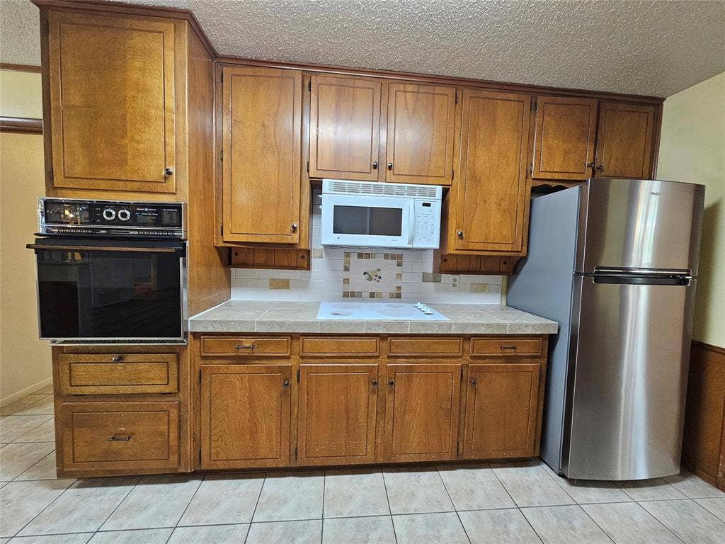 1109 W Redbud Drive, Hurst, TX 76053 Wood-finish cabinetry, tile flooring, built-in oven, stainless steel refrigerator, and microwave