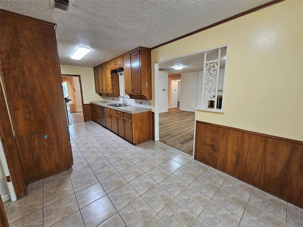 1109 W Redbud Drive, Hurst, TX 76053 Tile flooring and paneling detail in the kitchen, featuring wood cabinetry, stainless-steel sink, and a built-in dishwasher