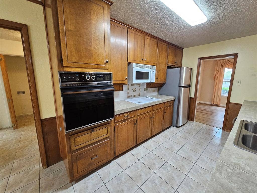 1109 W Redbud Drive, Hurst, TX 76053 Wood-finish cabinetry, tile flooring, built-in oven, stainless steel refrigerator, and a built-in microwave