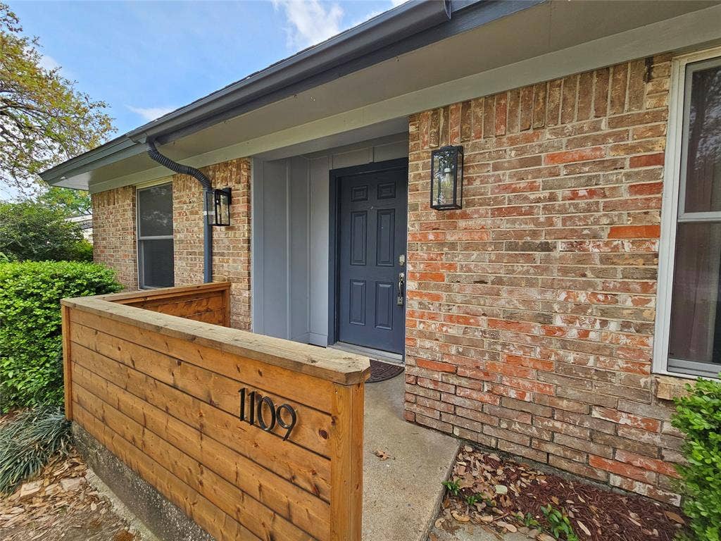 1109 W Redbud Drive, Hurst, TX 76053 Brick facade with contrasting dark trim, dark entry door, and two exterior wall sconces