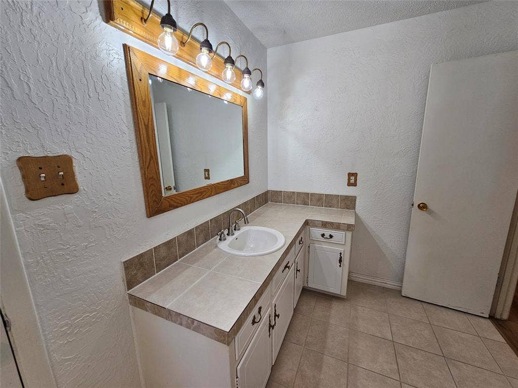 1109 W Redbud Drive, Hurst, TX 76053 White vanity with a drop-in sink, chrome faucet, and tile countertop