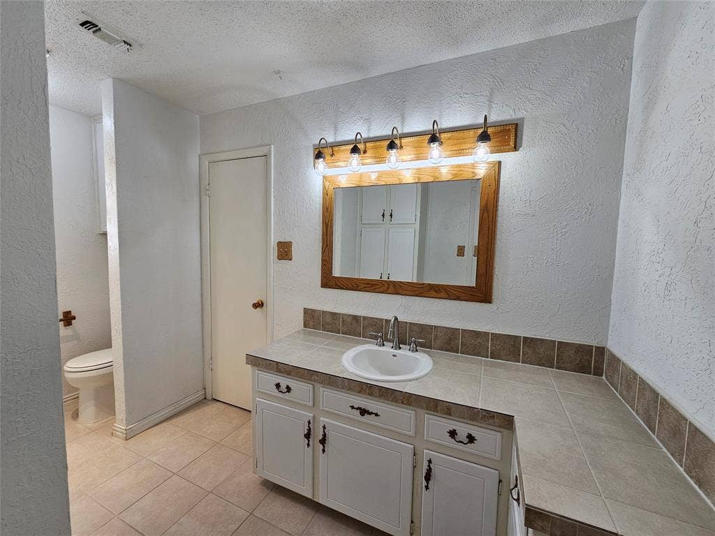 1109 W Redbud Drive, Hurst, TX 76053 Vanity with integrated sink, tile countertop, and wood-framed mirror