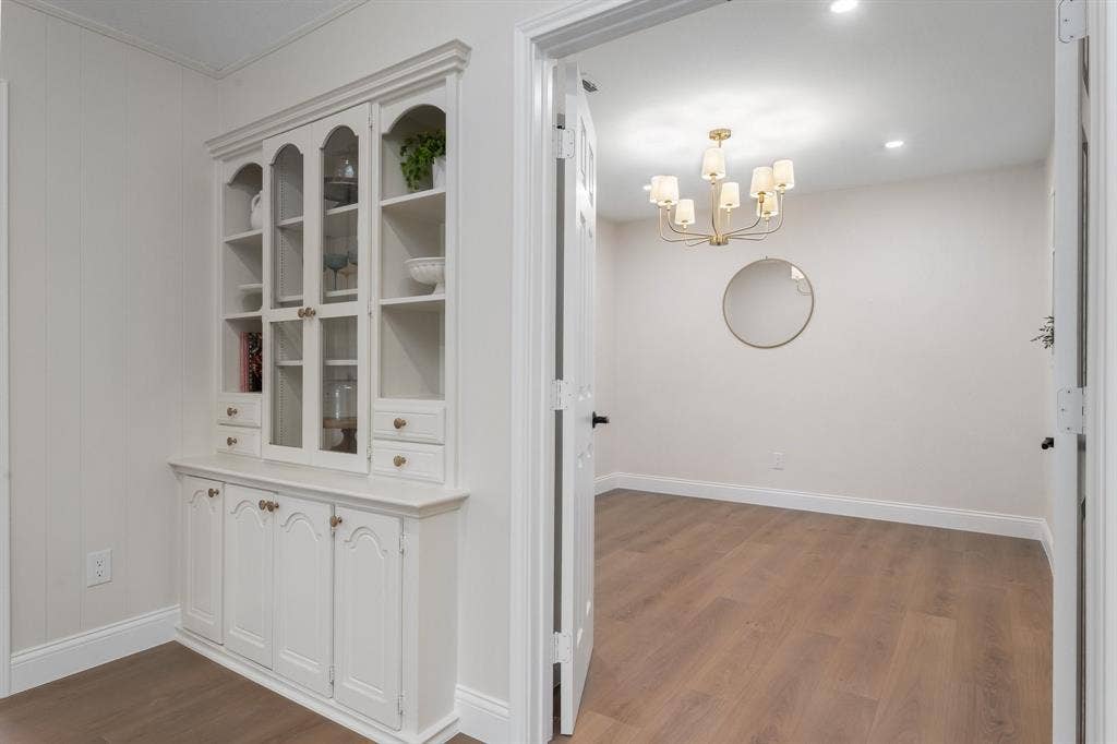2844 Hurstview Drive, Hurst, TX 76054 Built-in display cabinetry with glass fronts and lower storage, wood-finish flooring, recessed lighting, and a multi-arm chandelier