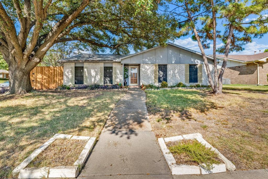 1715 Cherokee Trail, Plano, TX 75023 Single-story residence featuring a light-colored brick exterior, a gabled roofline, and mature trees providing shade