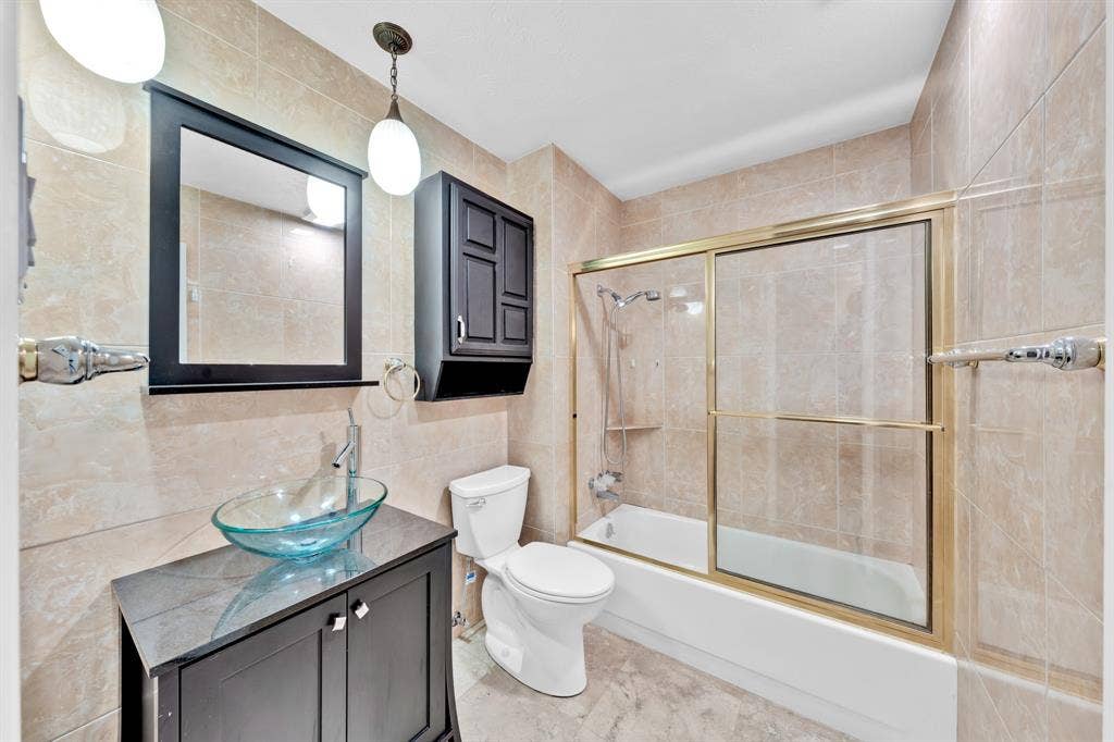 1715 Cherokee Trail, Plano, TX 75023 Bathroom featuring full-height tiled walls, a glass vessel sink, dark wood-finish vanity, and a shower-tub combination with sliding glass doors