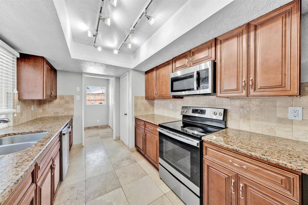 1715 Cherokee Trail, Plano, TX 75023 Kitchen featuring abundant cabinetry, stone-finish countertops, stainless steel appliances, a double basin sink, and track lighting