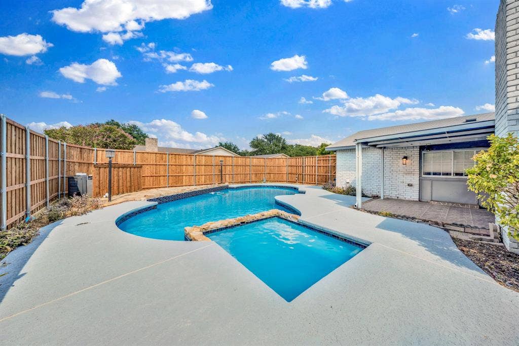 1715 Cherokee Trail, Plano, TX 75023 Backyard featuring a freeform swimming pool with integrated spa, expansive concrete decking, privacy fencing, and a covered patio area