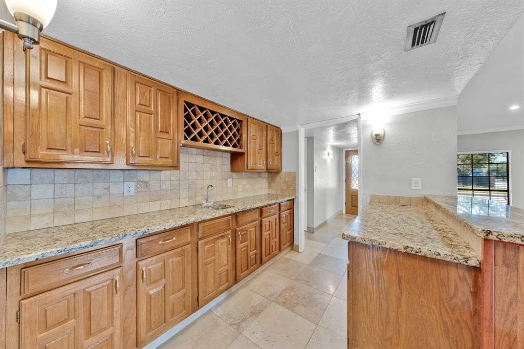 1715 Cherokee Trail, Plano, TX 75023 Wood-finish cabinetry with a built-in wine rack, light-toned tile backsplash, and granite countertops
