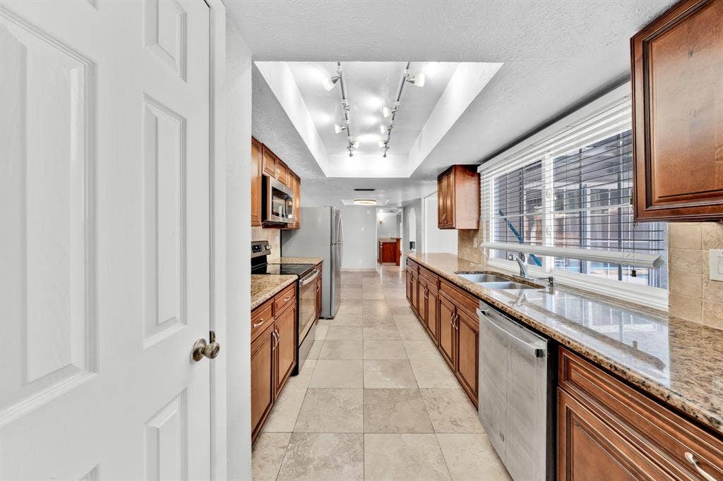 1715 Cherokee Trail, Plano, TX 75023 Galley kitchen featuring wood cabinetry, stone countertops, stainless steel appliances, and tiled flooring