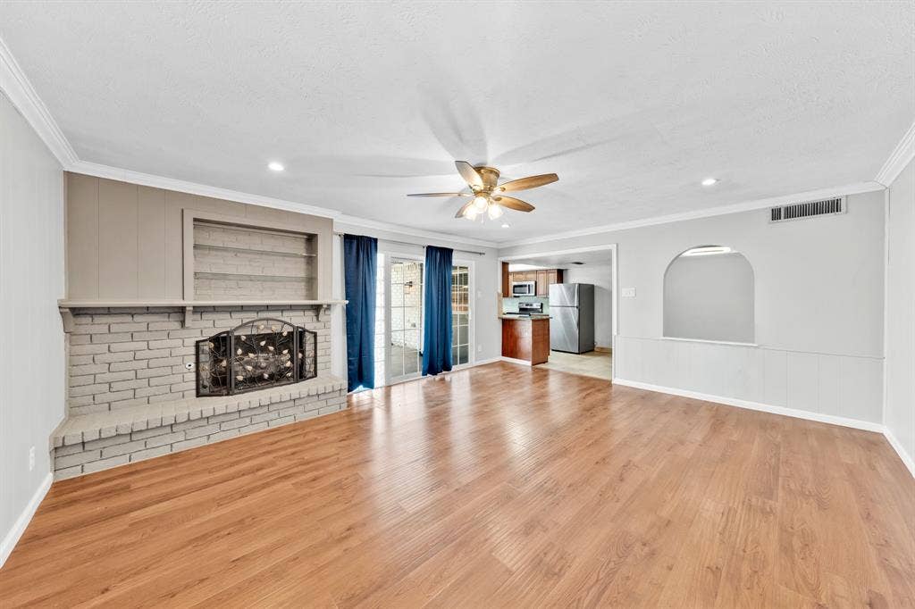 1715 Cherokee Trail, Plano, TX 75023 Wood-finish flooring, brick-faced fireplace with built-in shelving, ceiling fan with integrated lighting, recessed lighting, and a pass-through arched opening