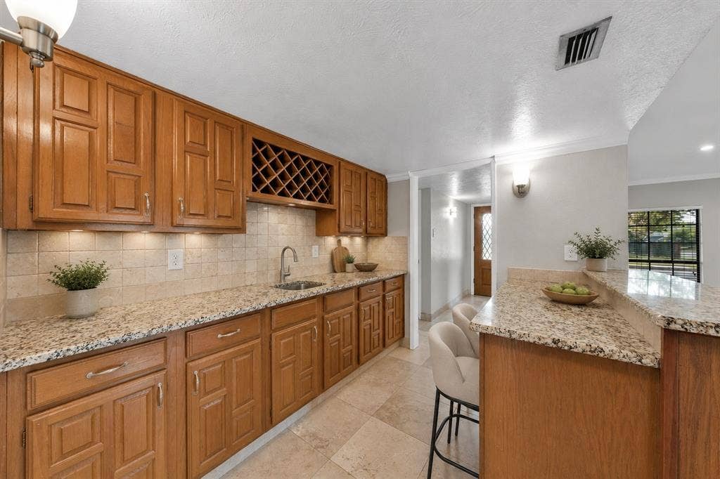 1715 Cherokee Trail, Plano, TX 75023 Wood-finish cabinetry with a built-in wine rack, stone tile backsplash, granite countertops, and an undermount sink