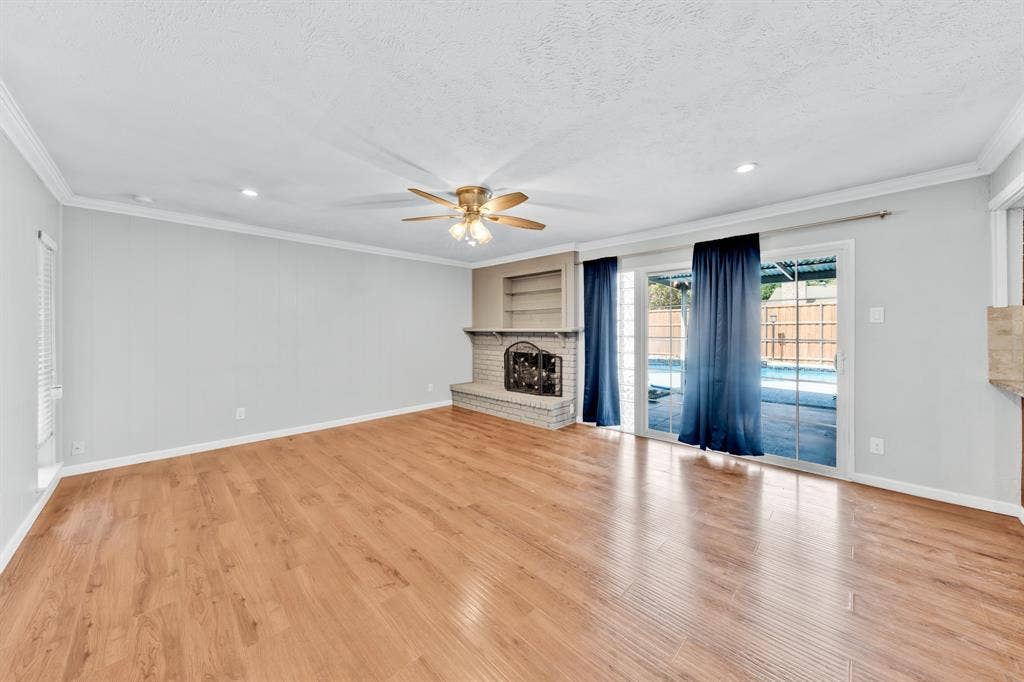 1715 Cherokee Trail, Plano, TX 75023 Spacious living area featuring wood-finish flooring, a brick fireplace with built-in shelving, and a ceiling fan