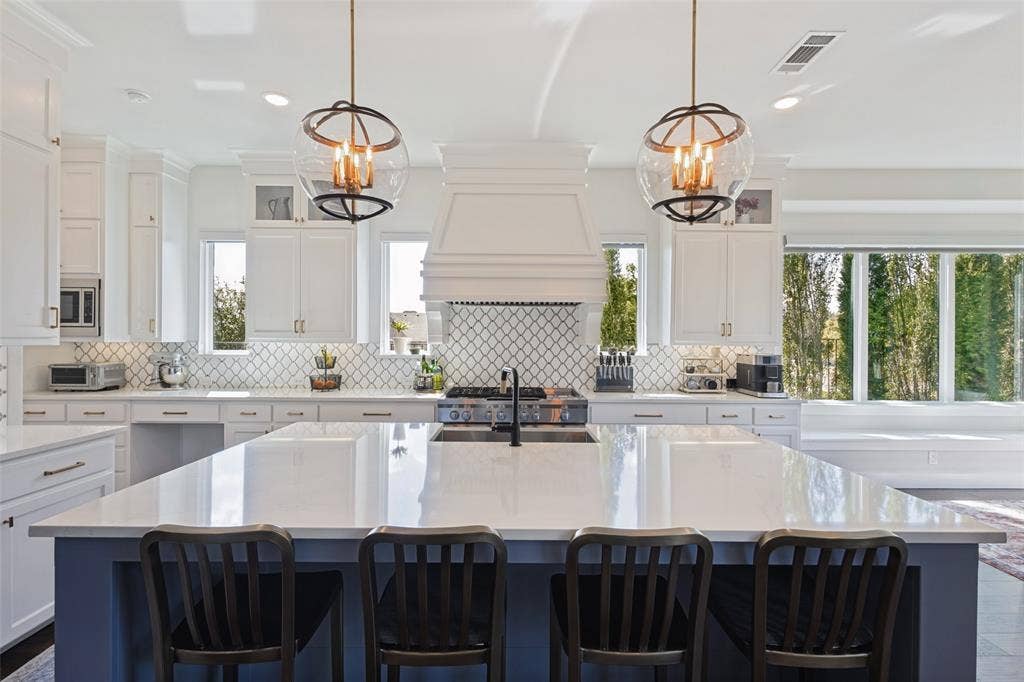 15018 Crape Myrtle Road, Frisco, TX 75035 Spacious kitchen with a large island, white cabinetry, integrated range hood, patterned tile backsplash, and oversized windows