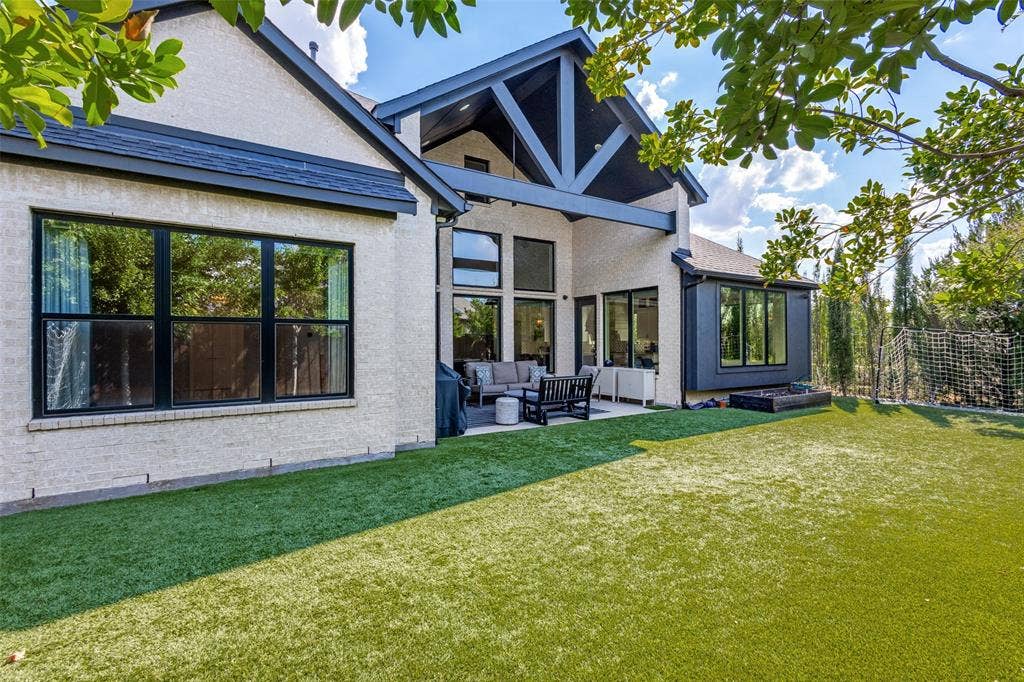 15018 Crape Myrtle Road, Frisco, TX 75035 Expansive artificial turf backyard featuring a covered patio, exposed beam architectural accents, and multiple large windows