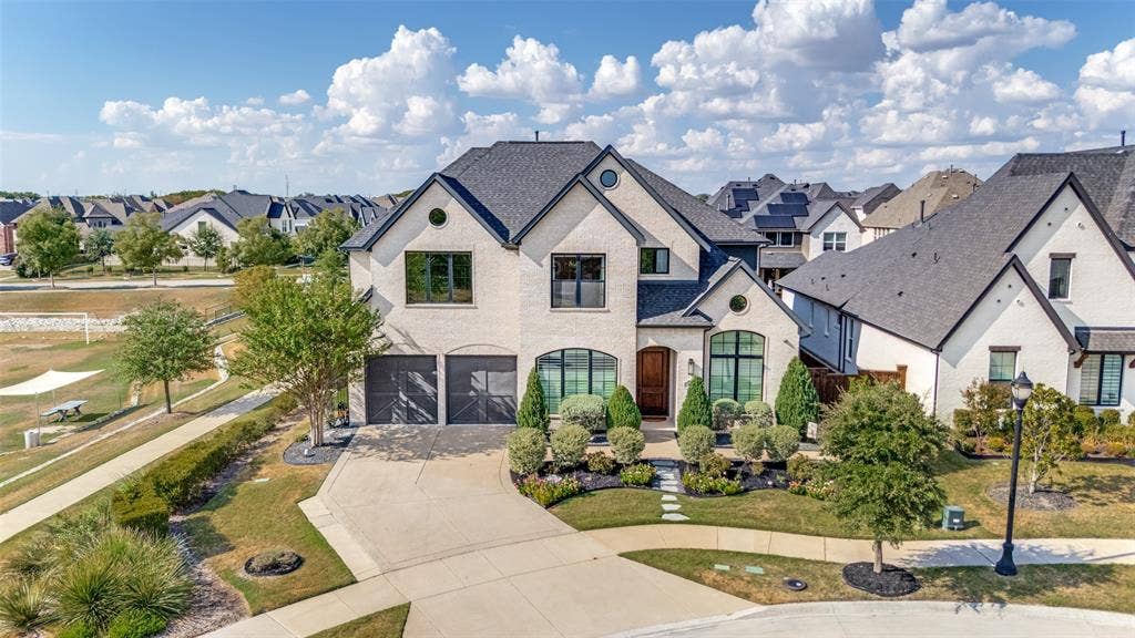 15018 Crape Myrtle Road, Frisco, TX 75035 Light-colored brick exterior with a dark shingled roof, arched entryways, a solid wood front door, and a two-car garage