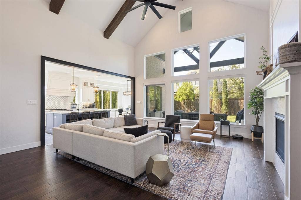 15018 Crape Myrtle Road, Frisco, TX 75035 Vaulted ceiling with exposed wood beams, expansive floor-to-ceiling windows, dark wood-finish flooring, and a built-in fireplace with a white mantel