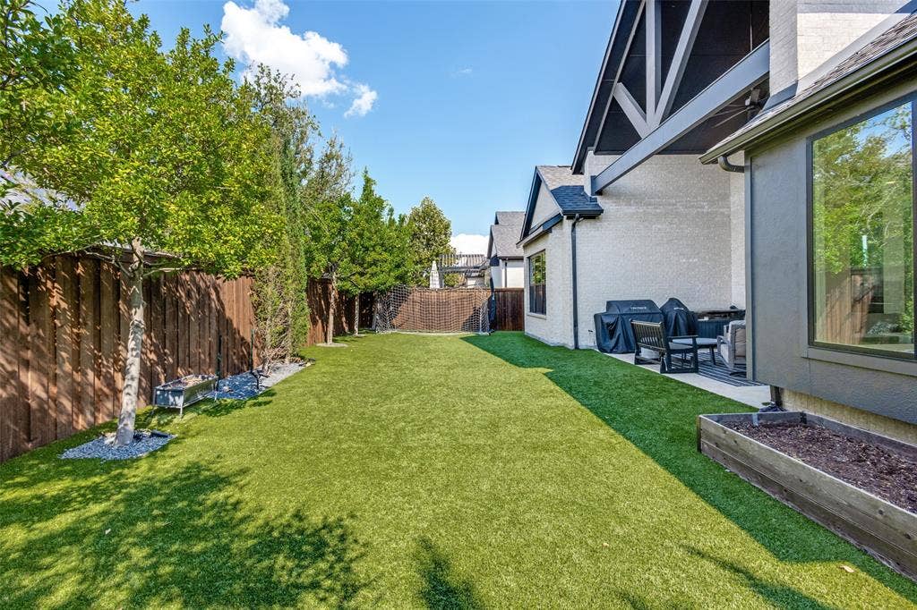 15018 Crape Myrtle Road, Frisco, TX 75035 Expansive backyard featuring artificial turf, wood fence, mature trees, and a raised planter box