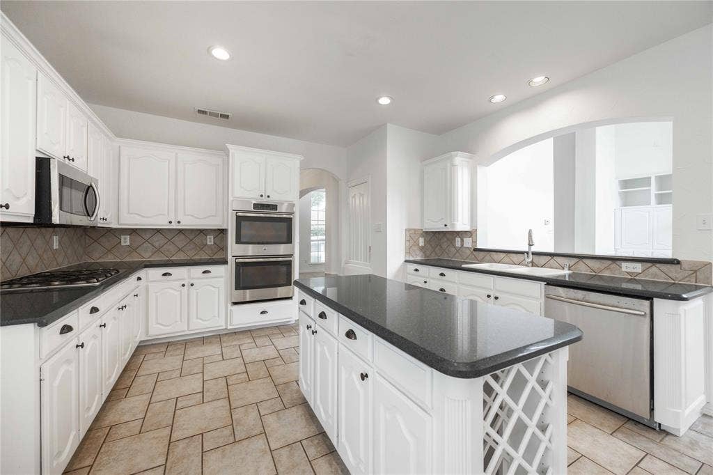 3305 Estacado Lane, Plano, TX 75025 White cabinetry with black hardware, dark countertops, a stainless steel double oven, and tiled flooring