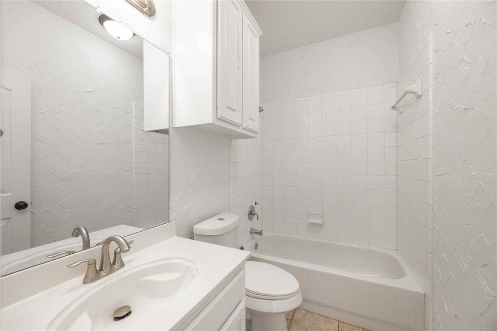 3305 Estacado Lane, Plano, TX 75025 White vanity with integrated sink, brushed nickel faucet, wall-mounted mirror, white shaker-style cabinetry, and a full bathtub with white subway tile surround