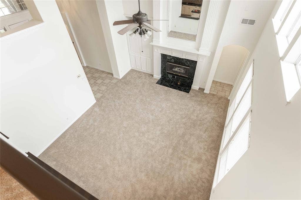 3305 Estacado Lane, Plano, TX 75025 Two-story living area with high ceilings, large windows, fireplace with dark stone surround, and ceiling fan