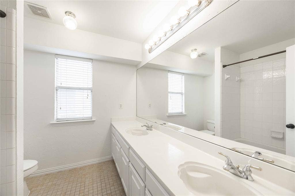3305 Estacado Lane, Plano, TX 75025 Dual vanity with integrated sinks, expansive mirror, a window with blinds, and white tile tub/shower combination