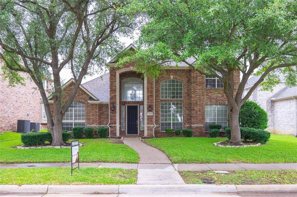 3305 Estacado Lane, Plano, TX 75025 Brick facade residence featuring mature trees, a manicured lawn, an arched window, and a prominent front entry