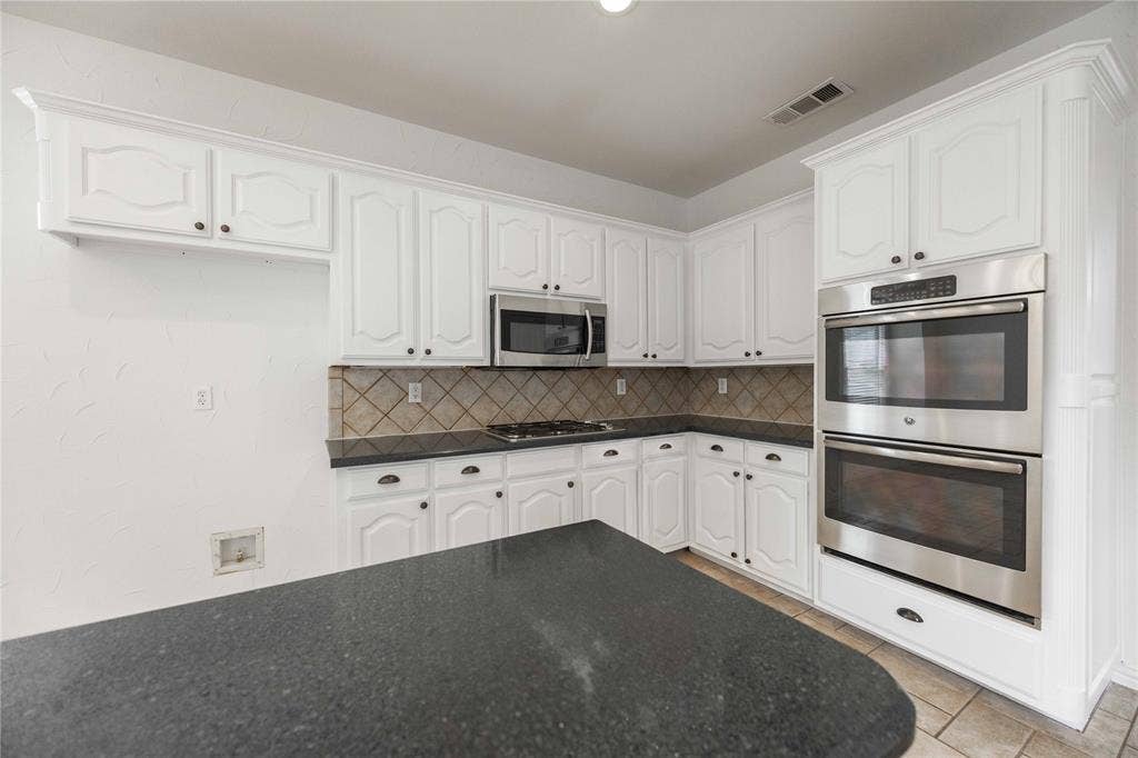 3305 Estacado Lane, Plano, TX 75025 White cabinetry, double wall ovens, stainless steel microwave, and dark countertops