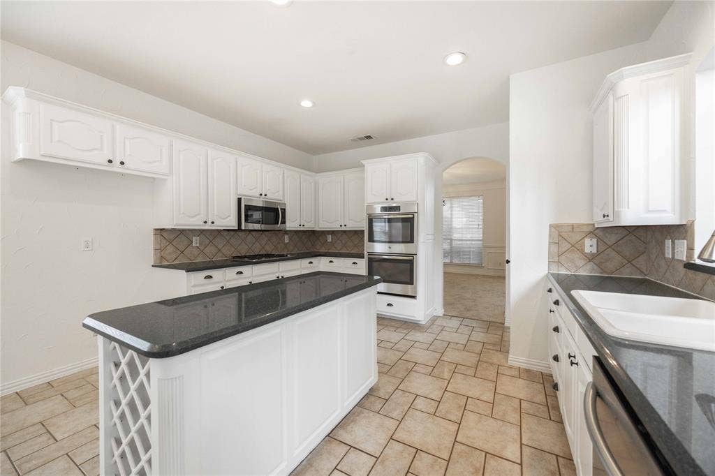 3305 Estacado Lane, Plano, TX 75025 White cabinetry with dark hardware, stone-finish countertops, stainless steel appliances, tiled backsplash, and tiled flooring