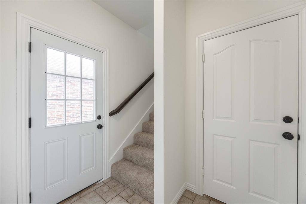 3305 Estacado Lane, Plano, TX 75025 Entryway featuring a paneled door with nine-lite glass, neutral tile flooring, and carpeted stairs with a dark wood handrail