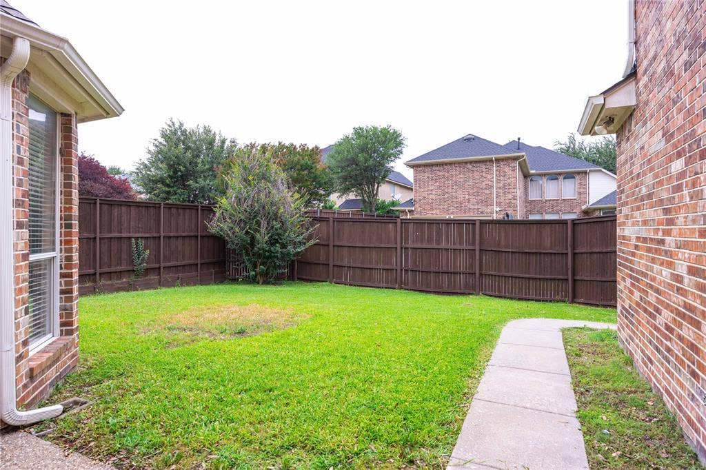 3305 Estacado Lane, Plano, TX 75025 Fenced backyard with a manicured lawn, concrete pathway, and mature landscaping