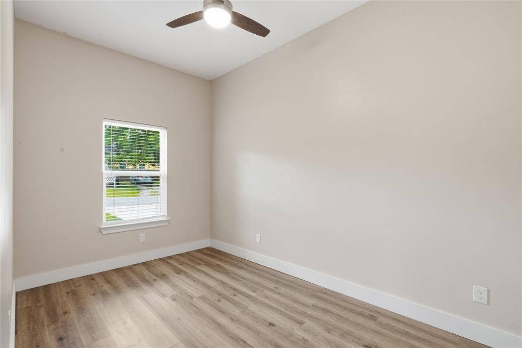Room featuring neutral wall tones, wood-finish flooring, a contemporary ceiling fan with integrated lighting, and a single window with horizontal blinds