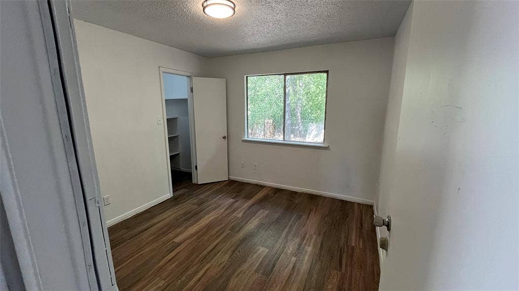 Bedroom 2 - Wood-finish flooring, overhead flush mount light fixture, window with exterior foliage, and built-in closet shelving