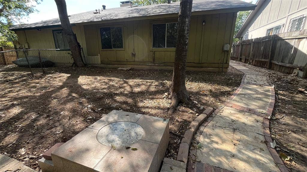 Rear exterior with multiple windows, mature trees, a stone-paved pathway with brick edging, and a built-in stone fire pit