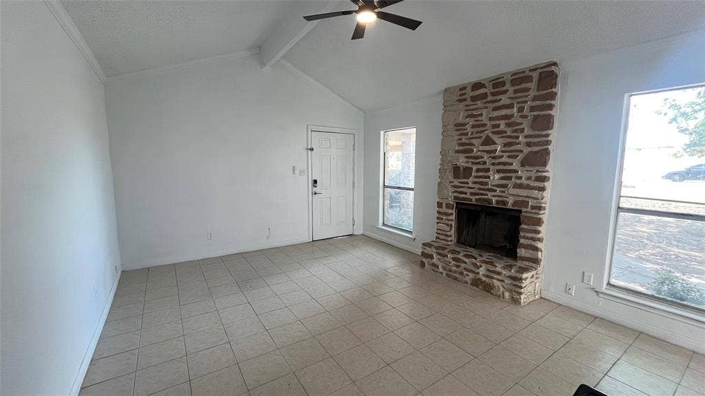 Vaulted ceiling with a ceiling fan, stone-clad fireplace, tiled flooring, and multiple windows