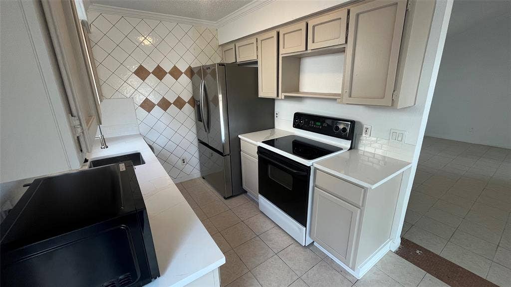 Updated kitchen featuring a stainless steel refrigerator, black electric range, light-toned cabinetry, and white countertops with a subway tile backsplash