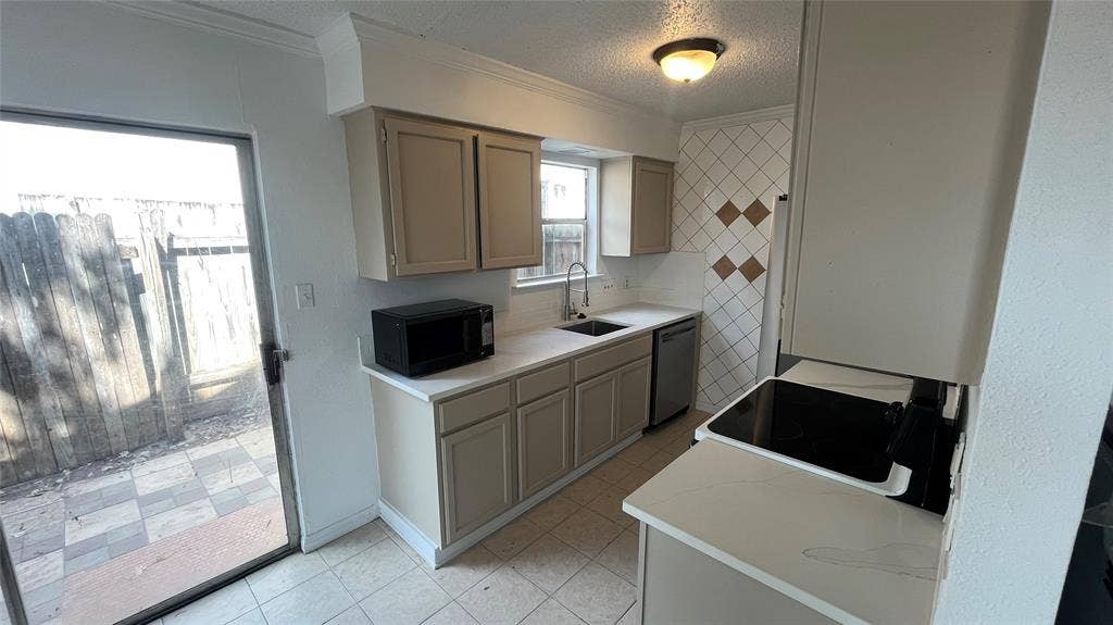Kitchen featuring light-toned cabinetry, solid surface countertops, stainless steel sink, and patterned tile backsplash