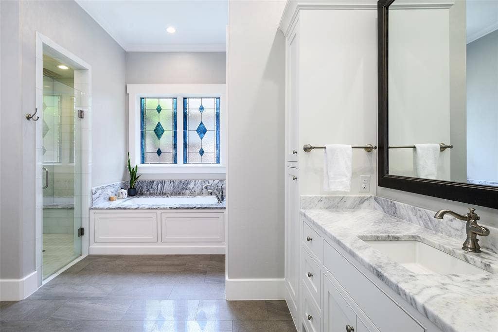 3420 Hanover Street, University Park, TX 75225 White vanity with stone countertop and integrated sink, glass-enclosed shower with tile surround, built-in storage cabinetry, and decorative stained-glass window