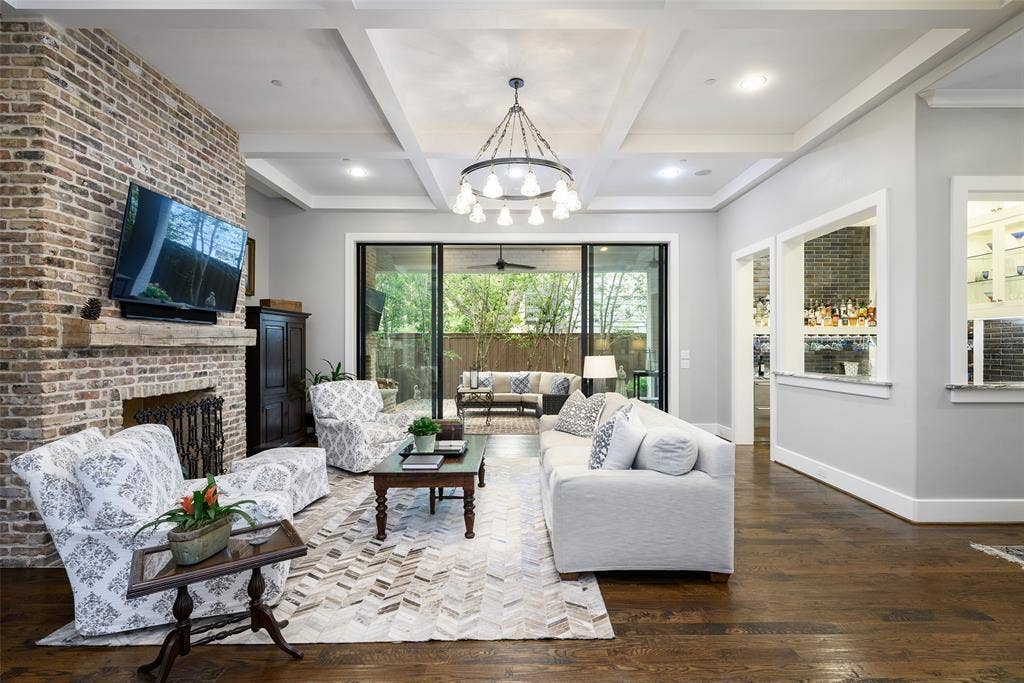 3420 Hanover Street, University Park, TX 75225 Exposed brick fireplace with a wood-beam mantel, dark wood-finish flooring, coffered ceiling, and sliding glass doors to outdoor hardscaping