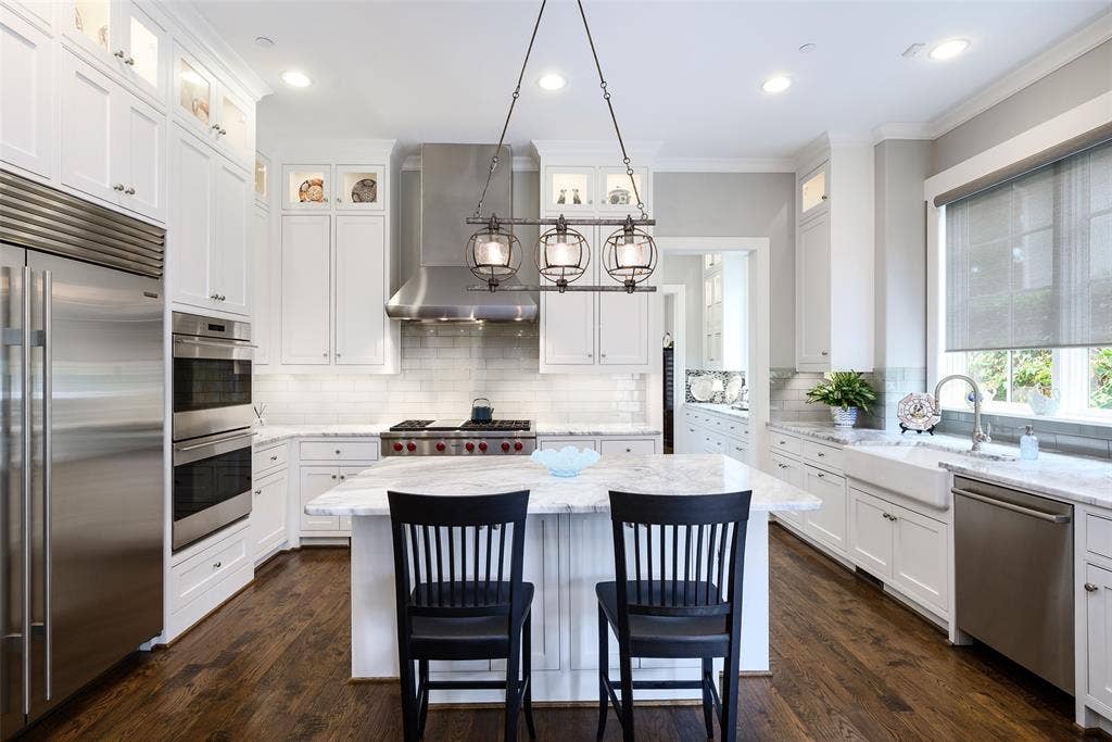 3420 Hanover Street, University Park, TX 75225 Gourmet kitchen featuring white cabinetry, stainless steel appliances, a center island with countertop seating, a farmhouse sink, and wood-finish flooring