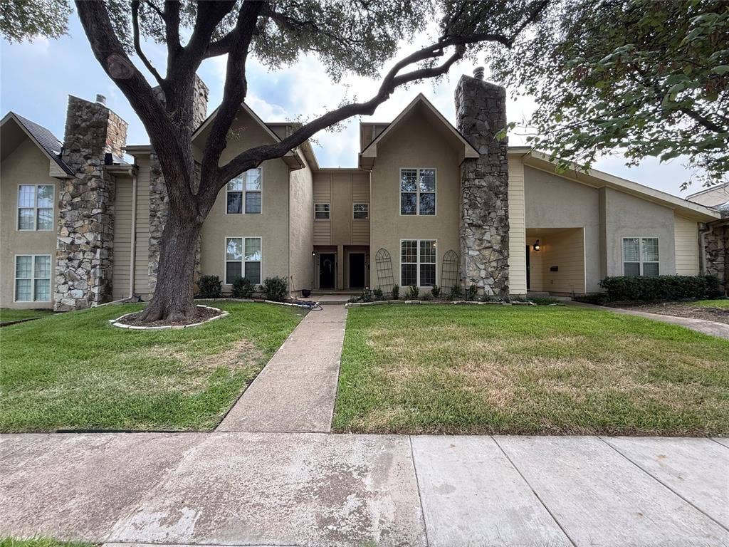 Two-story residence featuring stucco and stone veneer exterior, multiple gabled rooflines, and a concrete walkway
