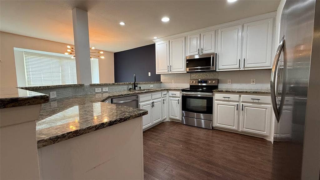 Kitchen featuring granite countertops, white cabinetry, stainless steel appliances, wood-finish flooring, and a tile backsplash