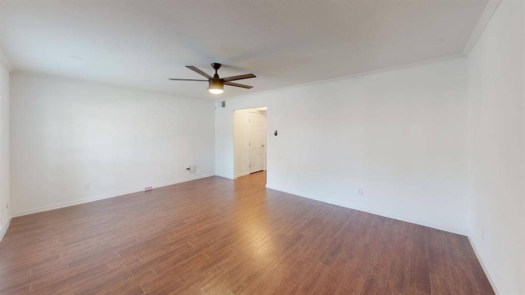 Spacious interior featuring wood-finish flooring, white walls, and a ceiling fan with integrated lighting
