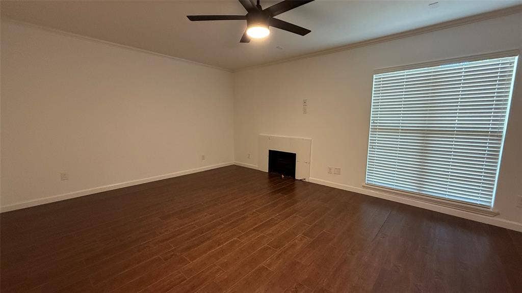 Expansive room featuring wood-finish flooring, a built-in fireplace, a large window with horizontal blinds, and a ceiling fan with integrated lighting